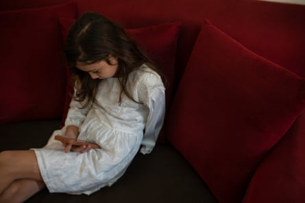 A girl in a white dress watches a video on a phone.