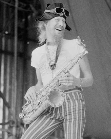 Nik Turner laughing on stage with a saxophone at a music festival