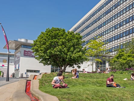 Students sitting and reading on grass outside a building with the words Sheffield Hallam University on the side
