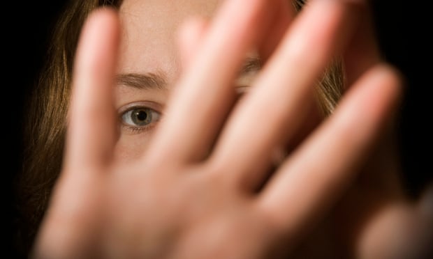 A woman holding her hand out in front of her looking a bit frightened, with a black background