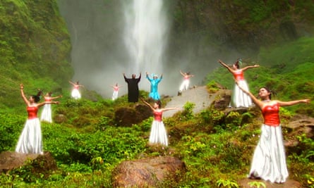 Performers stand in front of a waterfall, arms aloft