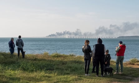 People watch a burning and partially damaged fuel tank on the Kerch Bridge in the Kerch Strait in Crimea.