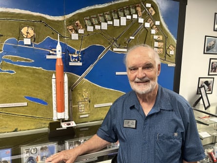 man in blue collared shirt smiles and stands by map with model rocket