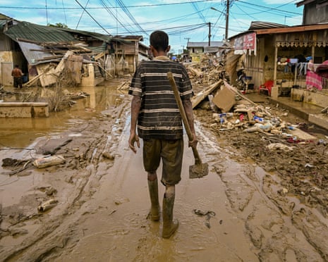 A man walks down a street covered in mud after flood waters receded