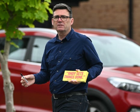 Burnham in glasses and a navy shirt holds a yellow campaign sign and pen while canvassing outdoors