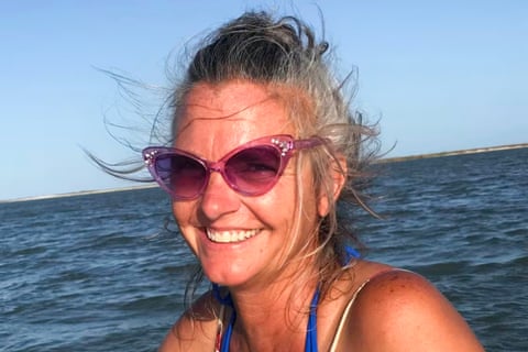 A middle-aged woman smiles with the ocean as a backdrop.