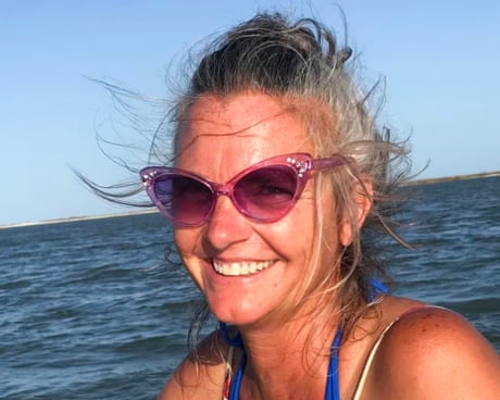 A middle-aged woman smiles with the ocean as a backdrop.