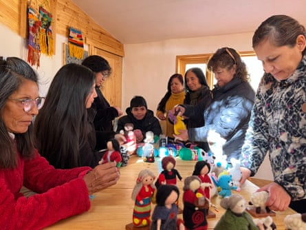 Seven Indigenous women around a table making woven dolls and animals.