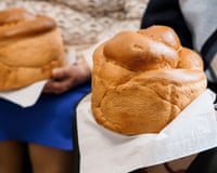 Two soft, golden brown Japanese milk bread loaves are carefully held in hands, wrapped in white paper