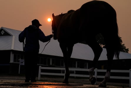 A handler leads a horse back into the stables as the sun is obscured by haze caused by the Canadian wildfires on Thursday at Belmont Park in Elmont, New York. Training was cancelled for the day due to poor air quality.