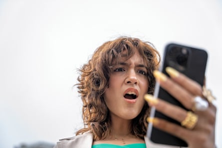A woman holds her phone and looks horrified as she views the screen