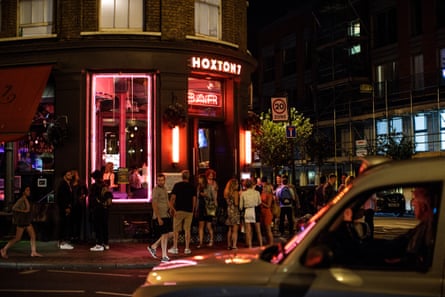 A taxi drives past people gathering outside a bar in Hackney in London.