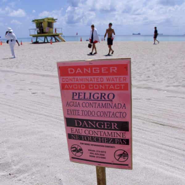 People pass by a sign on a beach warning of a sewage spill
