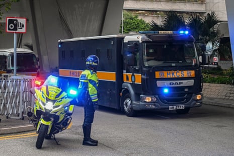 A police officer stands next to a motorcycle as a prison van passes