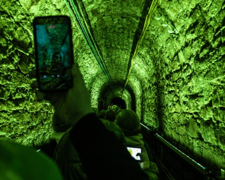Tourists photograph an underground tunnel during a boat tour of the Queen Luiza Mine. The tunnel is lit with green light