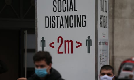 Masked people on the street in front of a social distancing sign