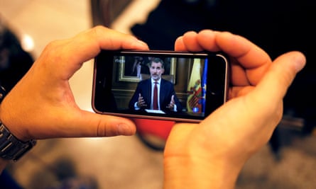 A man in Barcelona holds a mobile phone as he watches Spanish King Felipe making a televised address to the nation.