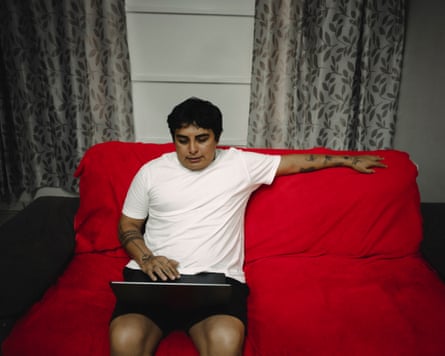 Júnio Hekurari sits on a red sofa, looking at a laptop on his lap