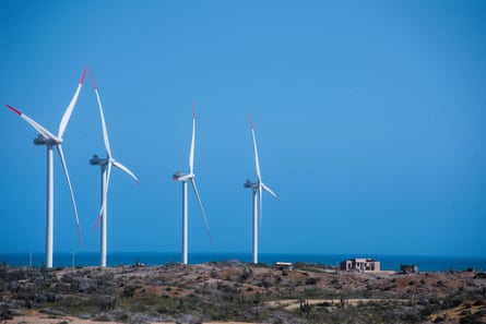 Four big wind turbines loom over a small building in some scrubby open land