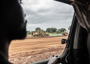 Mechanical diggers plough up land, in a photo taken through the window of a Jeep