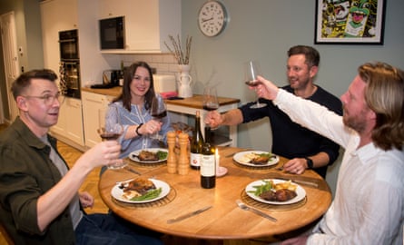 Four adults raise their glasses to cheers at a dinner table at home