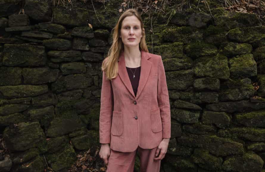 Amy Liptrot wearing a pink cord suit in front of a dry-stone wall in Yorkshire