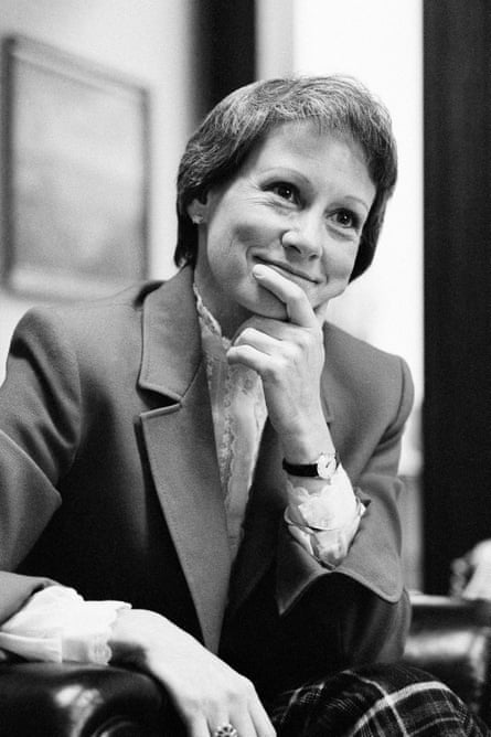 Black-and-white image of smiling woman in blazer reting her finger against her chin.