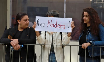 Three women stood behind railings, with the one in the middle holding up a banner with the message ‘free Nadera’ on it