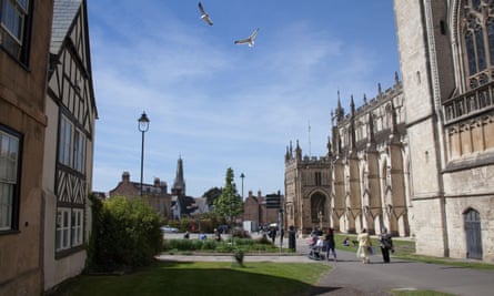 Two seagulls flying next to a wall of the Gloucester Cathedral on a sunny day