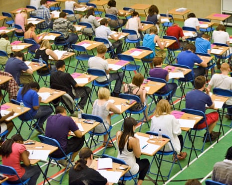 A-level students sit an exam at rows of individual desks inside a sports hall
