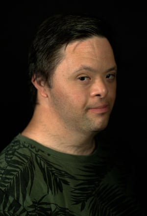 A portrait of a man looking straight into the camera in front of a black background.