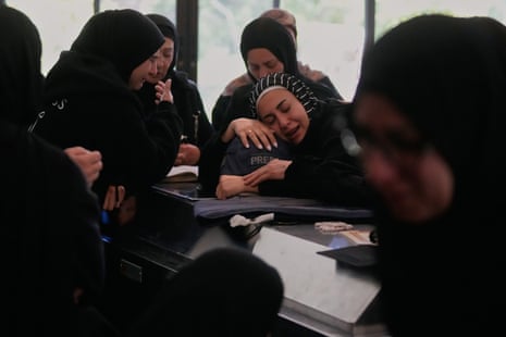 A woman hugs a press helmet over a coffin as other women console her.