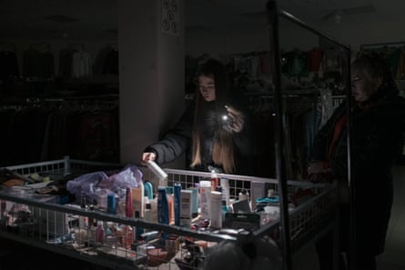 Young woman shining her phone torch on care and beauty products in a dark shop