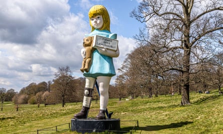 A colourful sculpture of a sad-looking girl with a brace on her leg and holding a teddy in one arm and a collection box in the other, surrounded by beautiful countryside