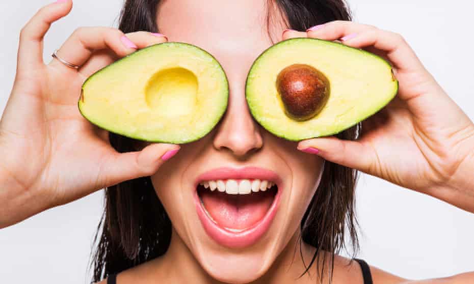Woman holding an avocado half in front of each eye