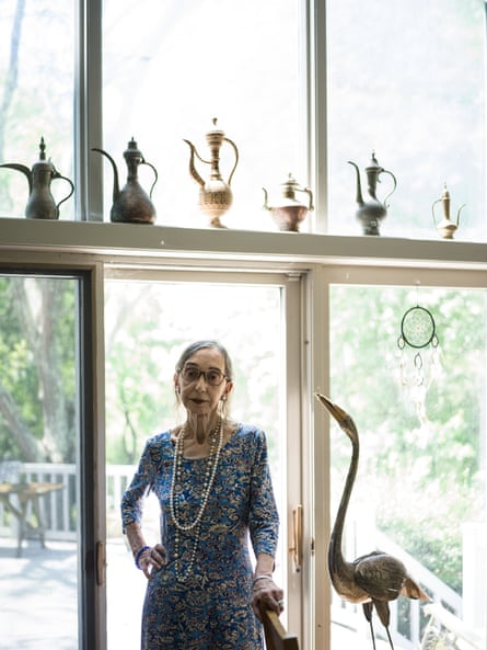 Oates stands in front of a glass-panelled door beside a sculpture of a bird with some eastern looking teapots arranged along a ledge above her