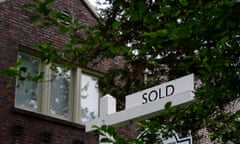 A picture of a black-on-white 'Sold' sign outside a brick home with a leafy green tree in front of it.