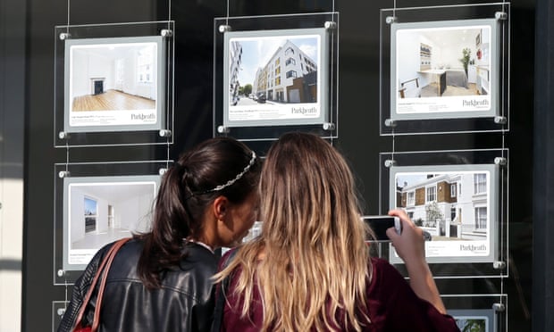 Two women look at houses for sale in an estate agent’s window.