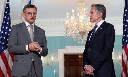 Dmytro Kuleba talking with Antony Blinken while standing in front of US flags in a room featuring an ornate chandelier