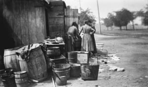 black and white photo of backs of two women standing outside by barrels