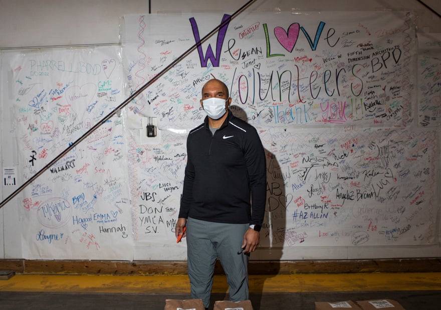 A man wearing a mask stands in front of a ‘we love our volunteers’ poster.