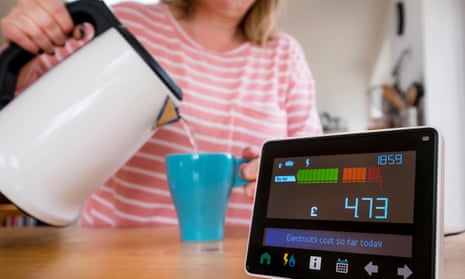 Energy monitor (smart meter) in the kitchen of a UK home as a woman makes a cup of tea