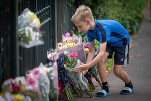 A child lays flowers against railing where other flowers have been left in a makeshift memorial