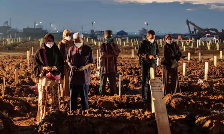 Relatives pray by the graves of Covid-19 victims during a funeral at cemetery in Jakarta