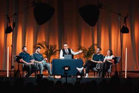 Five people sit on stage in front of a red curtain