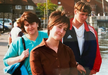 A middle aged woman in a turquoise top stands alongside a younger woman with a cropped hairdo and a young man in a tracksuit.