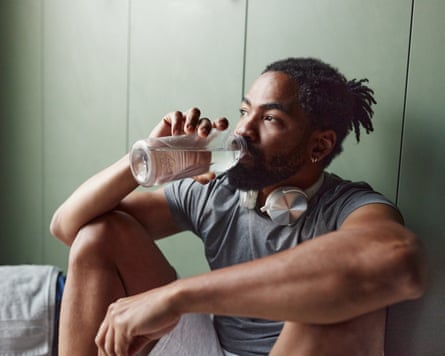 Black male athlete drinking water in the gym’s locker room.