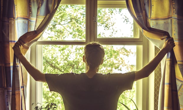 A young man opens curtains on a sunny day