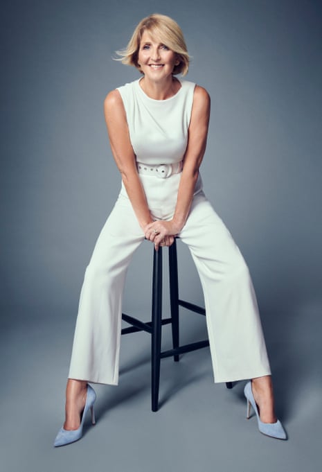 Kaye Adams sitting astride a high stool, wearing wide-legged cream trousers, a sleeveless cream top and pale blue heels