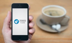 A man looks at his iPhone which displays the Tesco Mobile logo
